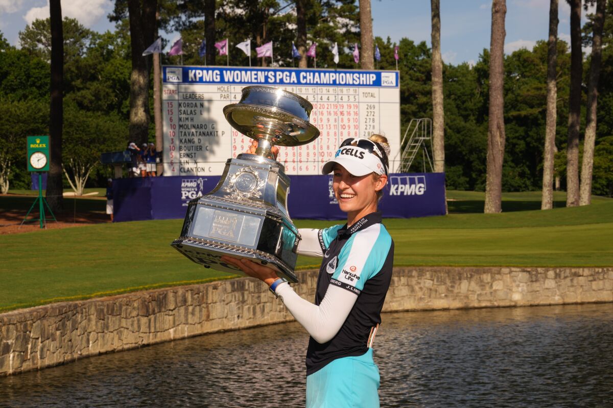 A woman golfer hoists a trophy.