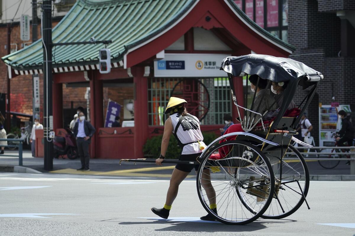 FILE - A rickshaw puller carries tourists near Sensoji Buddhist temple at Tokyo's Asakusa district in Tokyo, March 31, 2021. Japan’s government announced Tuesday, May 17, 2022, it will begin allowing small package tours from four countries in later this month before gradually opening up to foreign tourism for the first time since it imposed tight border restrictions due to the coronavirus pandemic. (AP Photo/Eugene Hoshiko, File)