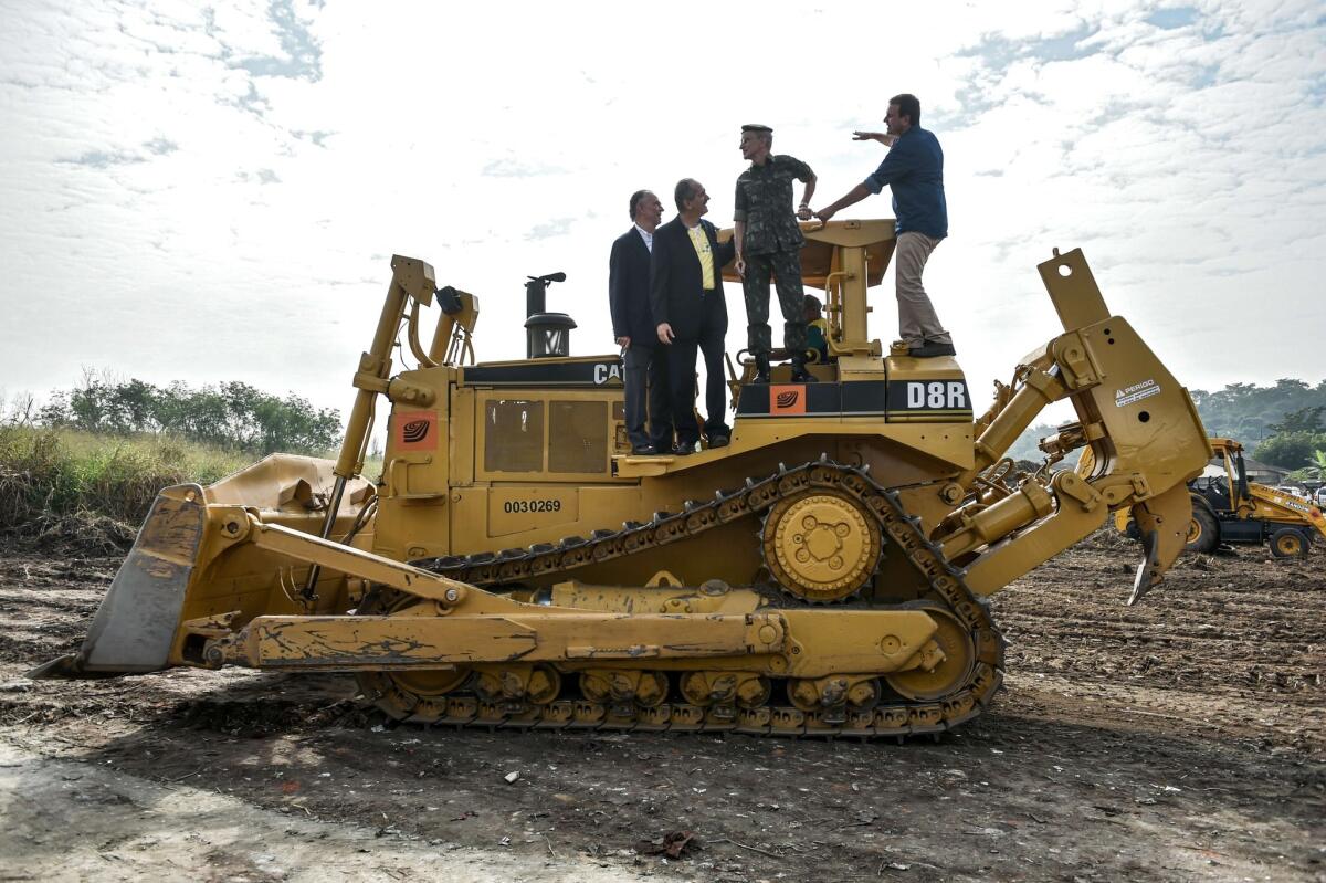 Mayor of Rio de Janeiro Eduardo Paes, right, Brazilian army commandar General Enzo Martins Peri, second from right, Brazilian Sports Minister Aldo Rebelo, second from left, and president of the Brazilian Olympic Committee, Carlos Nuzman, left, pose atop a bulldozer during a ceremony marking the opening of construction at Deodoro Olympic Park.