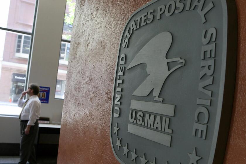A file photo shows a man walking by a sign in the lobby of a post office. A Santa Ana postal worker was accused of stealing thousands of credit cards.