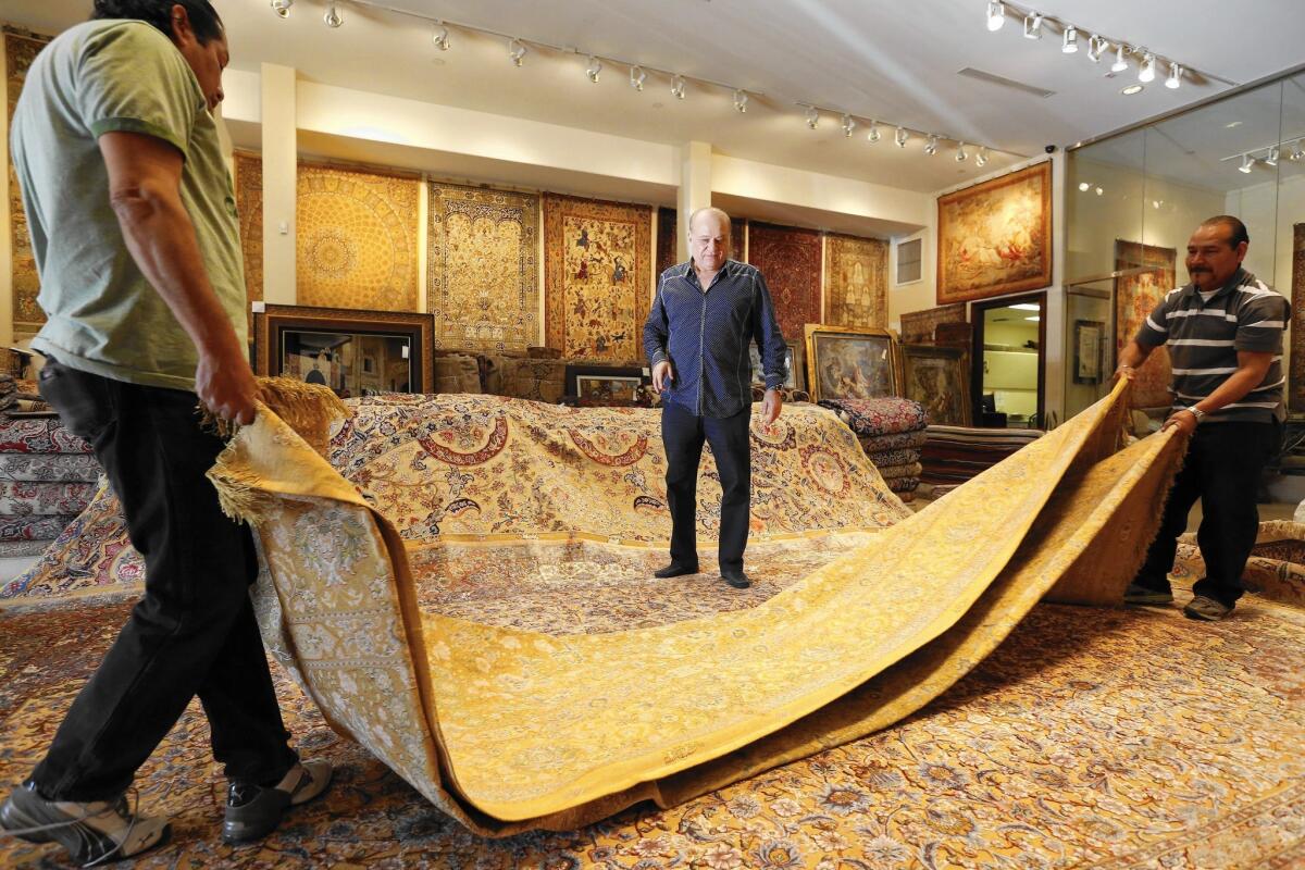 Alex Helmi, center, regards one of the 40 newly arrived handmade Persian rugs — some antique, some modern — at his Westwood store, Damoka.