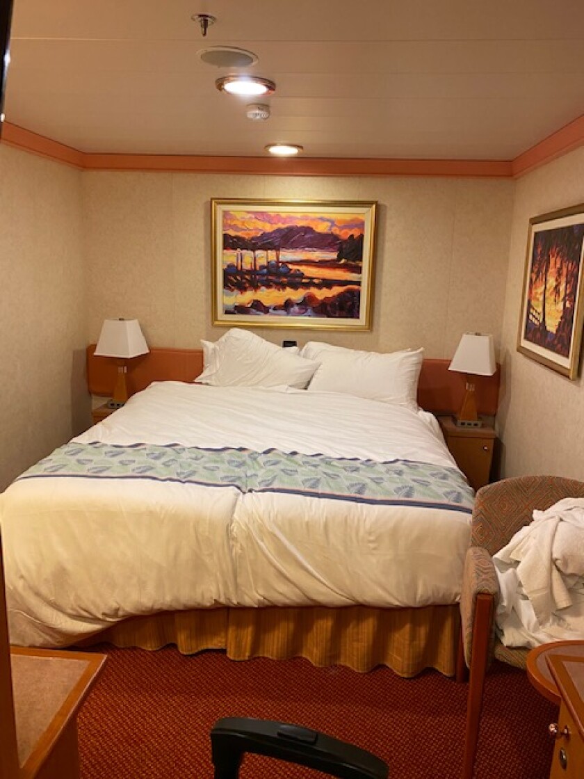A room on a cruise ship, with a queen-size bed.