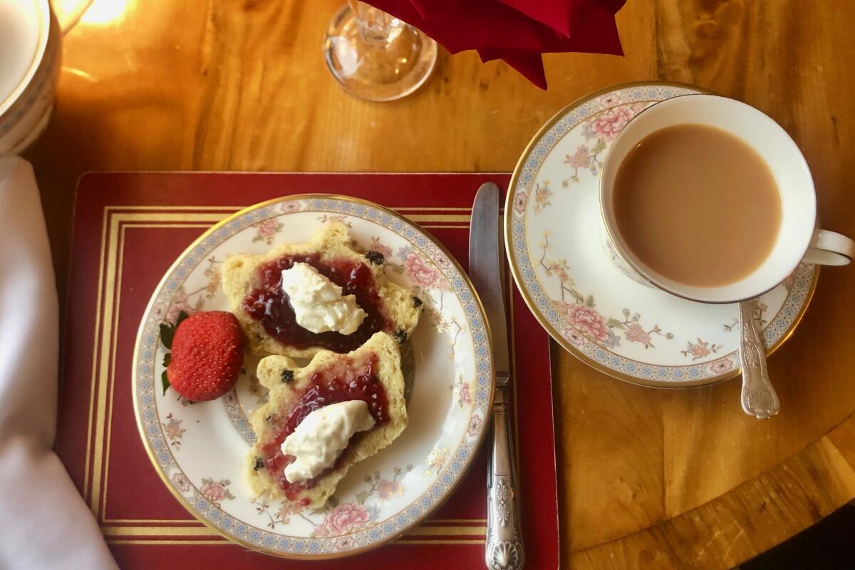 A cup of tea and a pastry with jam and clotted cream on floral china from Rose Tree Cottage.