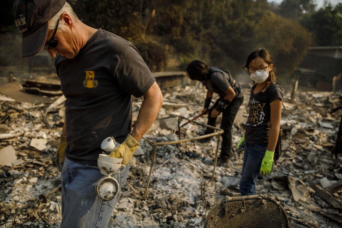 Jeff Lipscomb, left, Gabriel Lipscomb, 17, and Rachel Lipscomb, 11, look for items to recover in the wreckage of their burned home in Ventura.