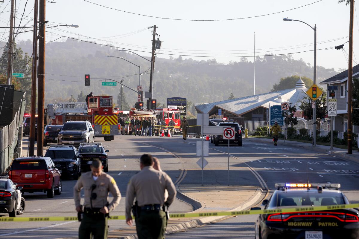 In view down the middle of two-way street, emergency crews walk along the cordoned-off street investigating a car accident.