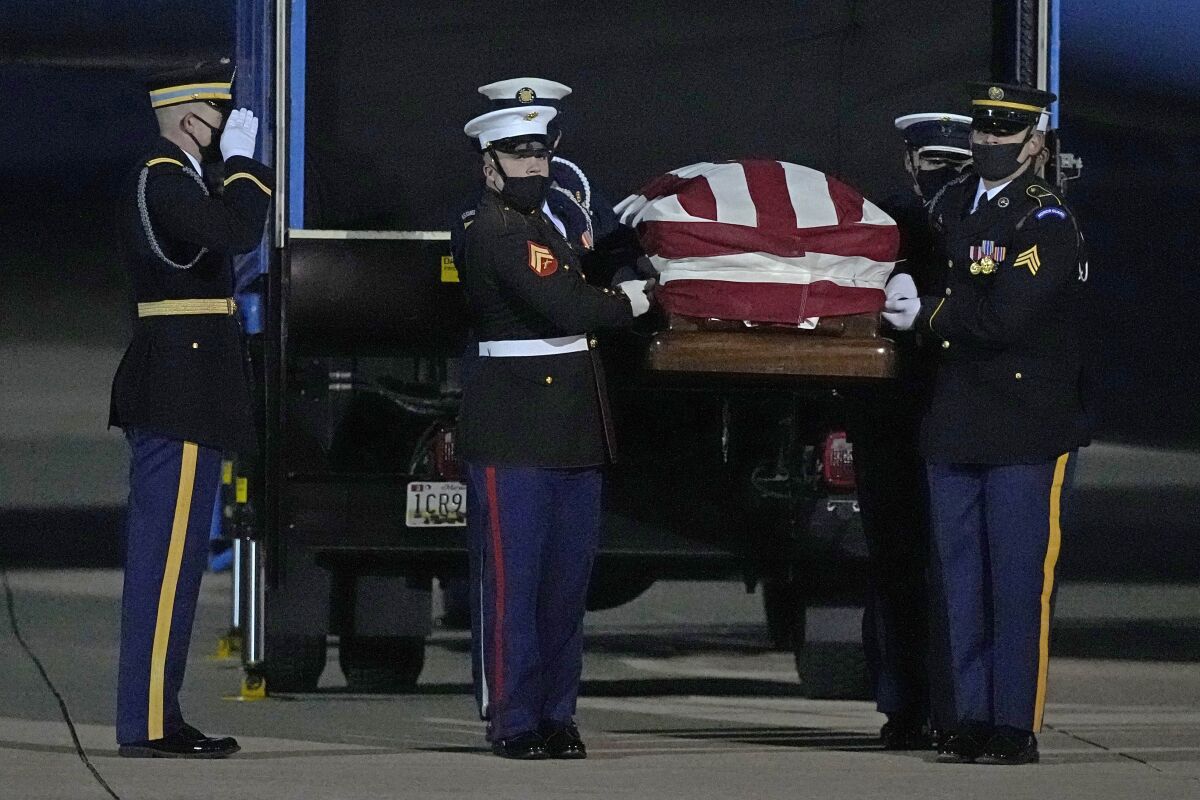 One service member salutes as others remove a casket, draped with an American flag, from a truck