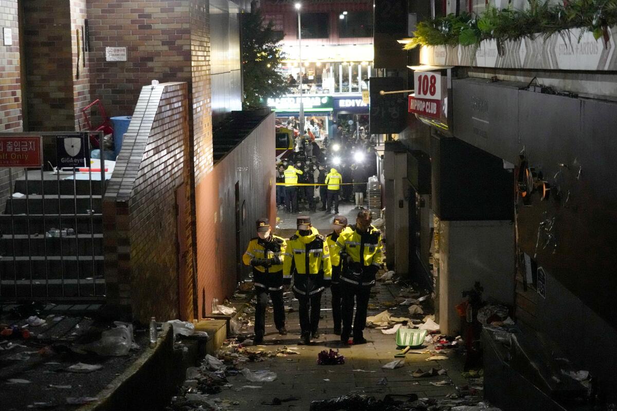 Police officers walk through a narrow alley full of trash.