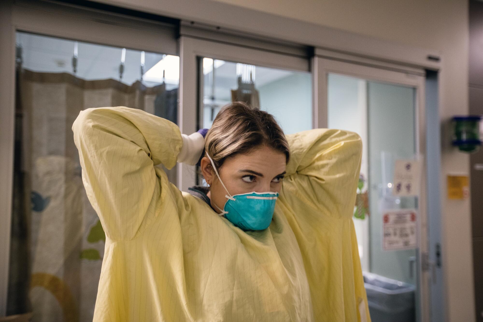 Nurse Mollie Perez, RN, ties her isolation gown on before entering a patient's room in the emergency department 