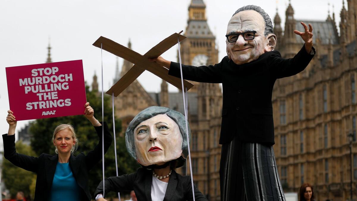 People wearing masks of Rupert Murdoch, right, and British Prime Minister Theresa May, stage a protest opposite Parliament in London on Thursday.