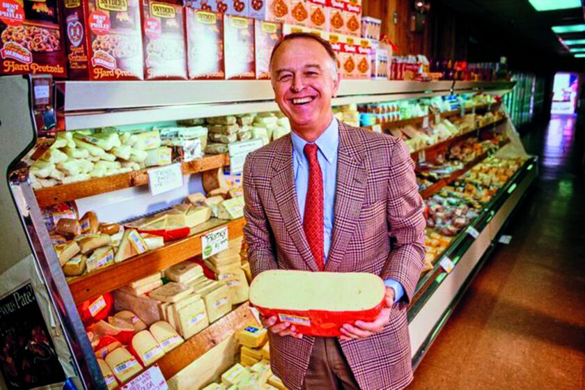 Joe Coulombe poses with a wheel of "Closed Eye Baby Swiss" in the cheese aisle in 1975 at Trader Joe's. 