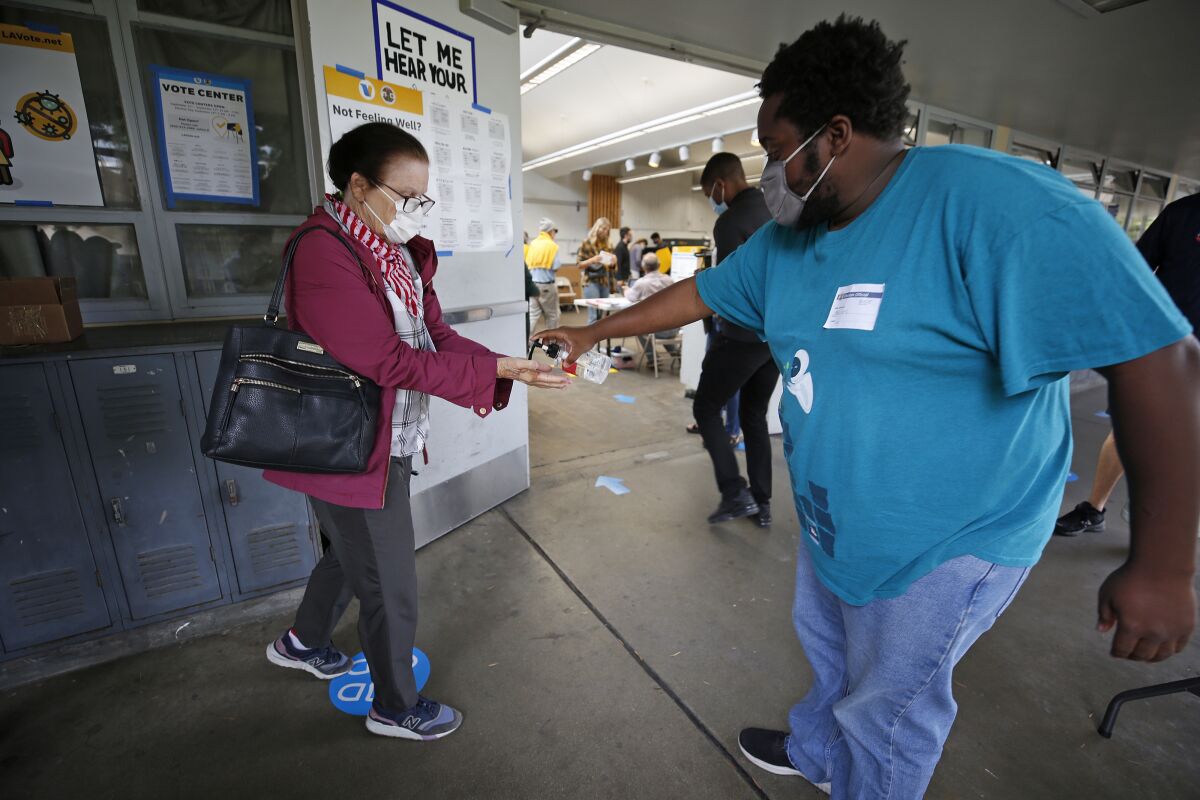 A poll worker squirts hand sanitizer onto the hands of a voter