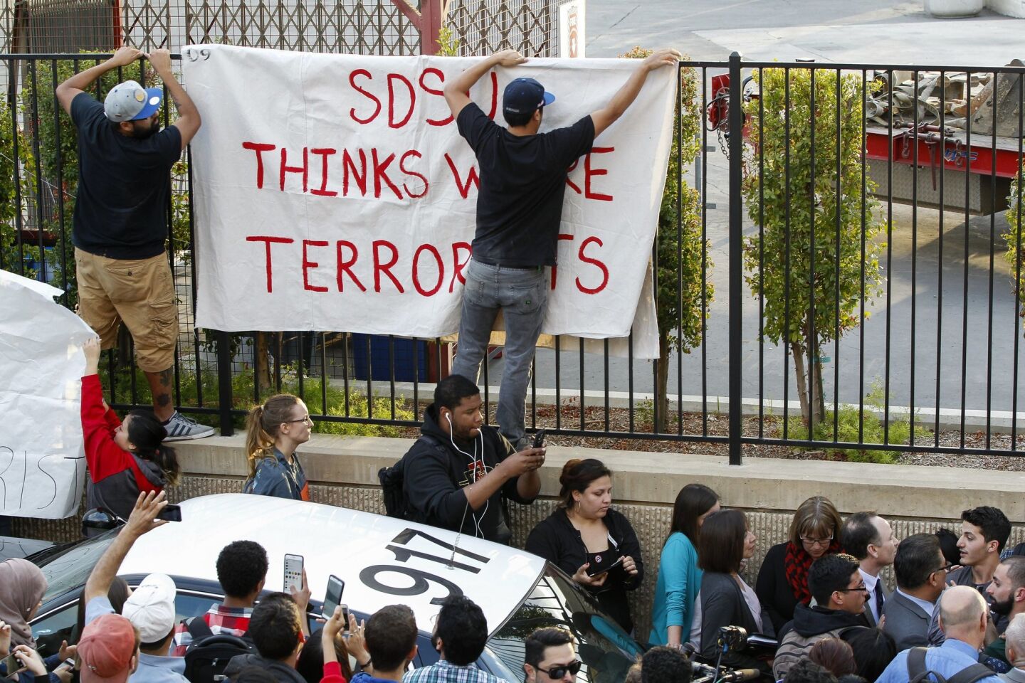 San Diego State students put up a sign as other students surround the SDSU president, lower right.