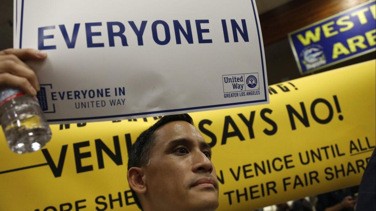 Len Nguyen shows his support for a planned emergency shelter at an open house at Westminster Elementary School last week. Behind him, others hold up a banner opposing the plan.