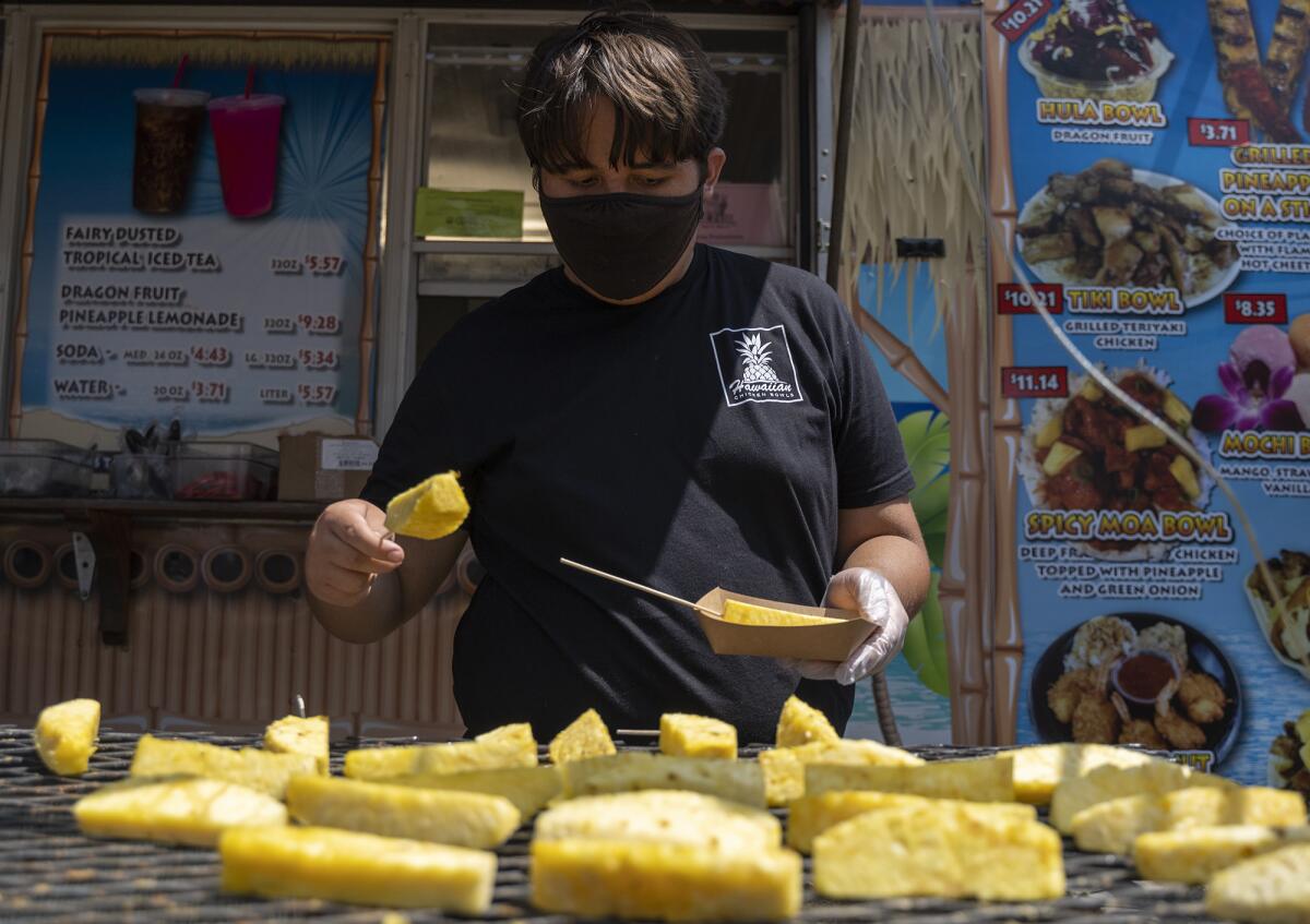 Jacob Fesili prepares grilled pineapple on a stick from the Hawaiian Chicken Bowls booth at the O.C. Fair on Thursday.