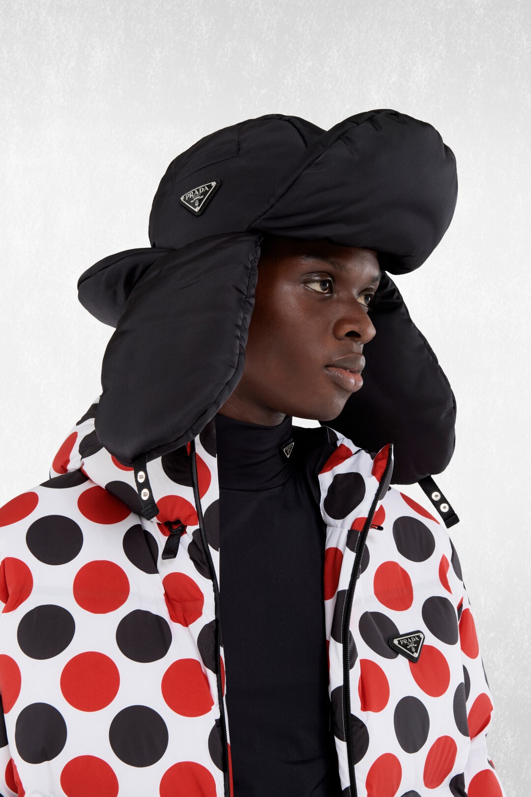 photo of Prada model wearing a black and red polkadot jacket and logo embellished black hat