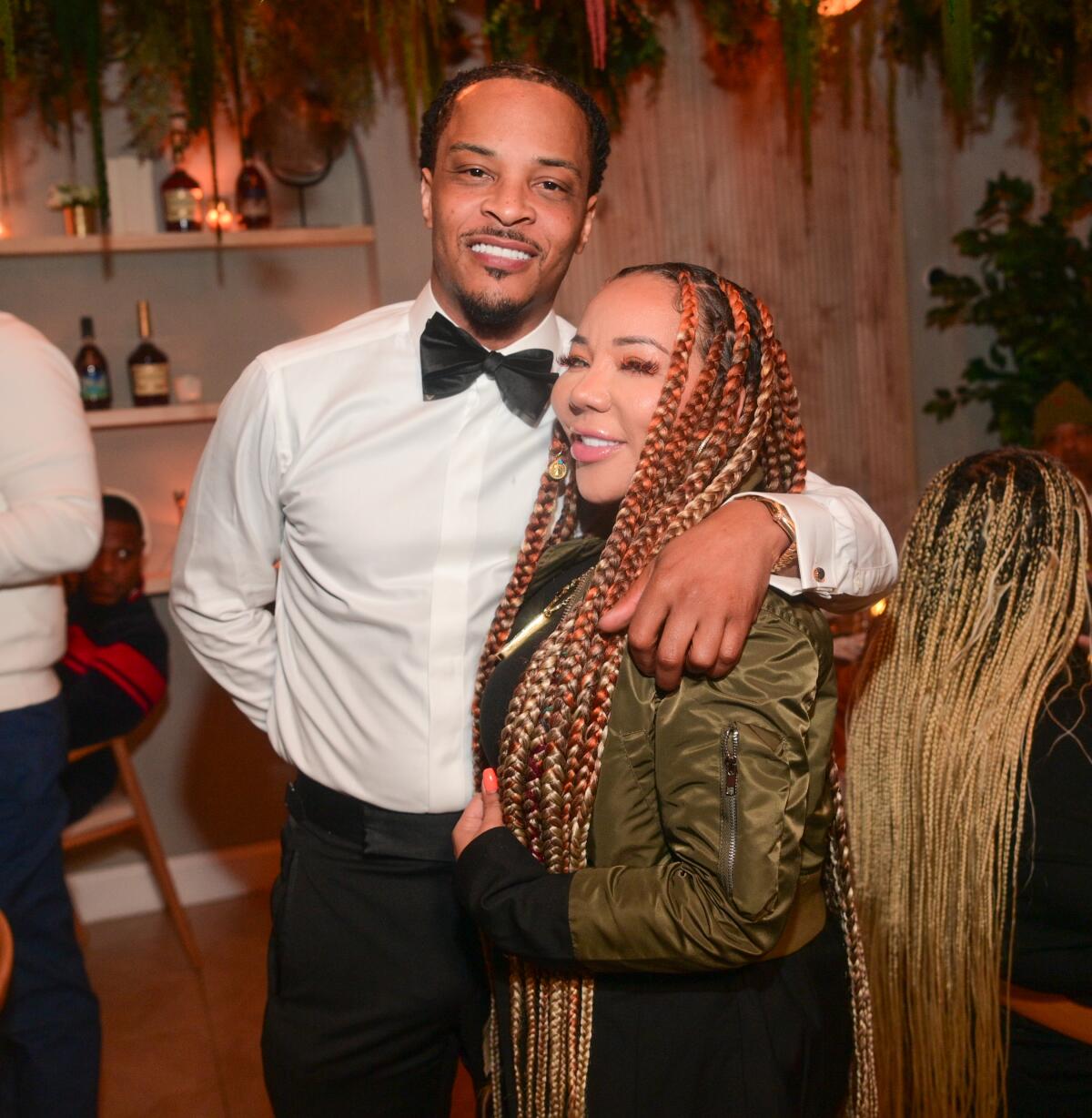 Tip "T.I." Harris in formalwear puts his arm around Tameka Harris who has long braids and a olive green bomber jacket