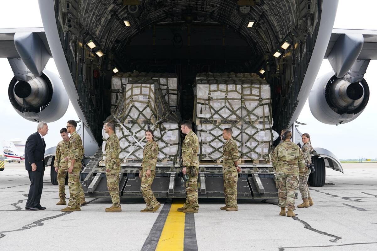 A man in a suit greets crew members of a C-17 that delivered a plane load of baby formula at an airport.