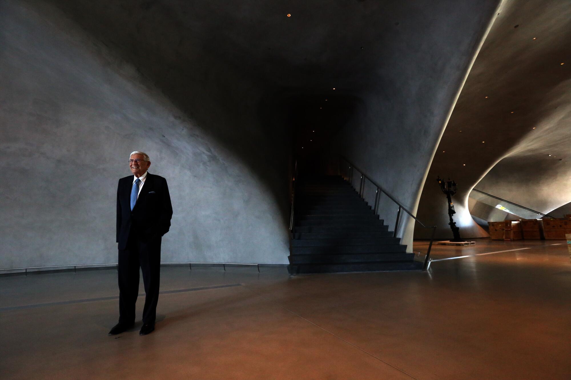 Eli Broad poses for a photo inside a cavernous space with curving, shadowed walls.