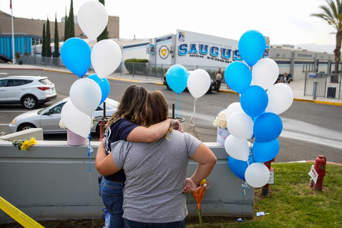 Hailey Stuart, a freshman at Saugus High School, and her sister Ashley Stuart hug after placing flowers outside the school on Friday.