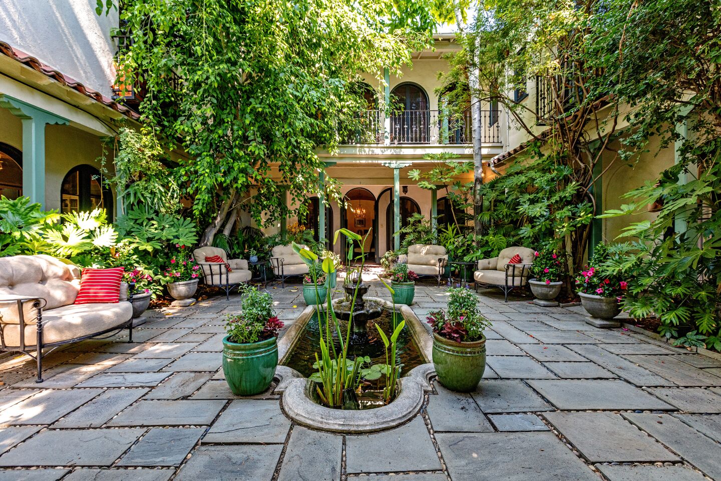The courtyard with furniture, plants and trees and stone flagstones in front of the house exterior.