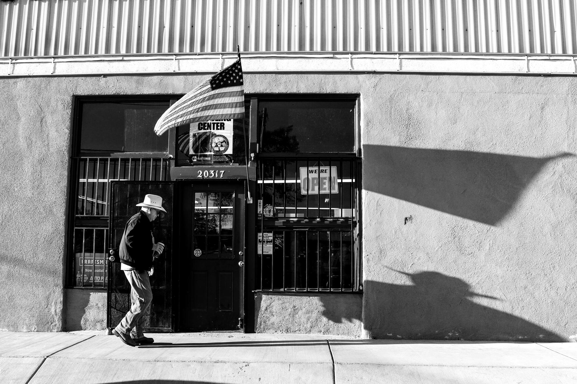 A man enters a doorway flanked by security bars in a storefront beneath an American flag.
