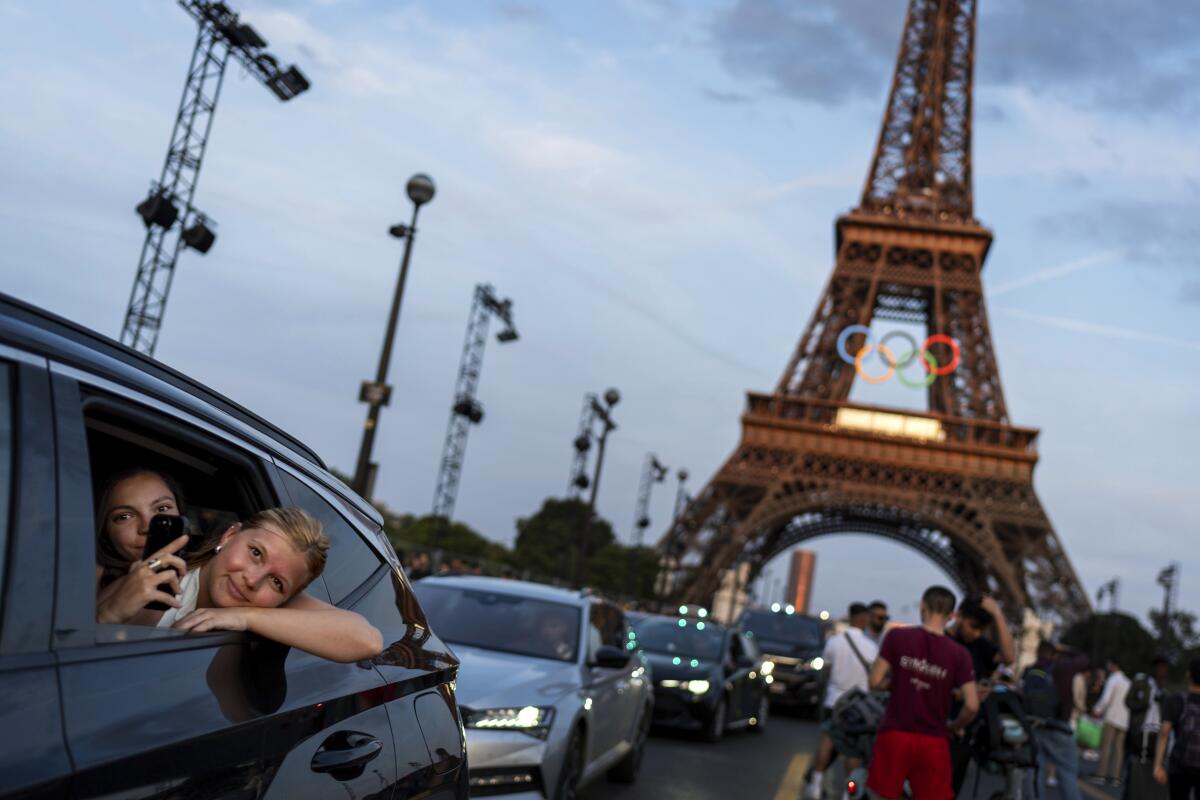 Passengers in the back of a taxi record themselves as they drive away from the Eiffel Tower decorated with the Olympic rings.