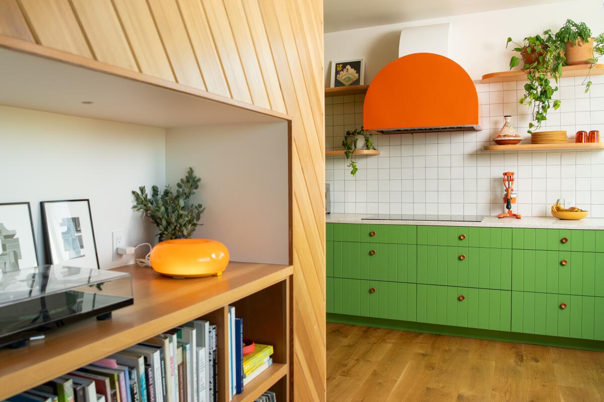A bookshelf and kitchen with green cabinets and orange hood