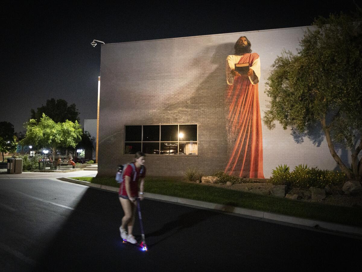 A person rides a scooter by a 30-foot "The Word" mural of Jesus Christ holding out a Bible.