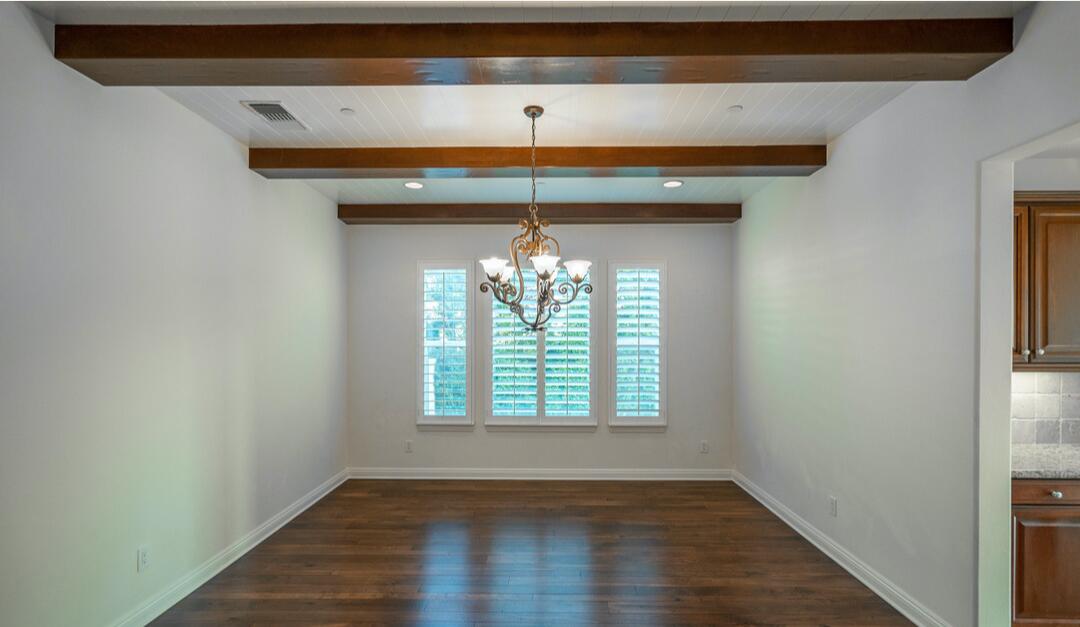 The dining room has wood floors and beams and a chandelier.