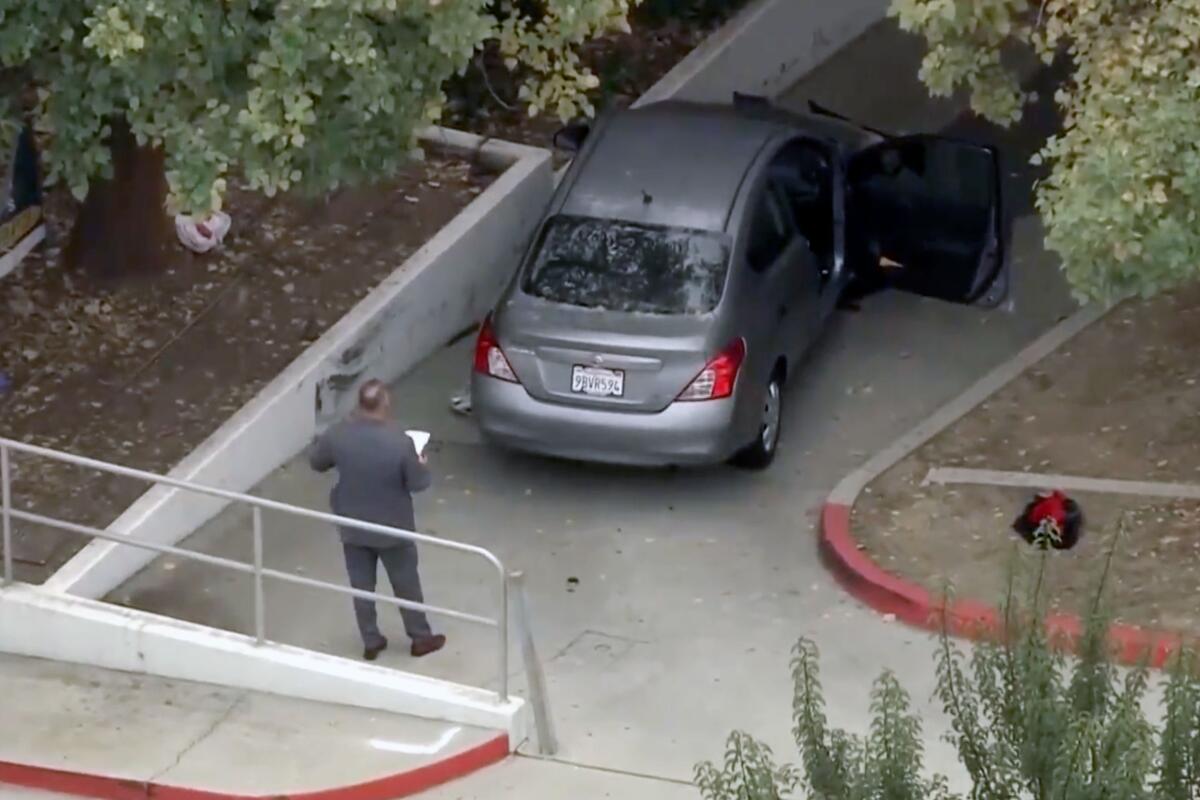 An investigator stands behind a crashed car with its doors open in an alleyway