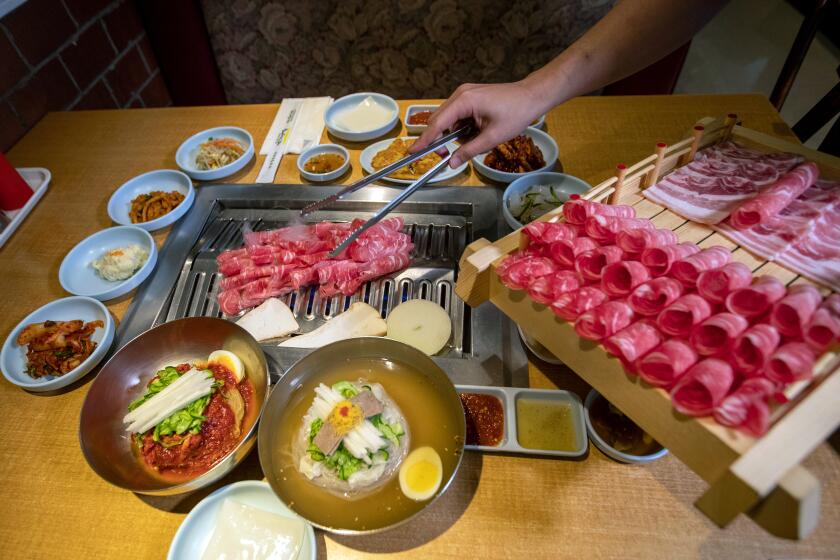 GARDEN GROVE, CALIF. -- WEDNESDAY, NOVEMBER 20, 2019: Korean BBQ beef brisket is cooked at the table at Mo Ran Gak Korean B.B.Q. in Garden Grove, Calif., on Nov. 20, 2019. In foreground is NK-style Bibbim Naengmyeon, left, and Moon Naengmyeon at right. (Allen J. Schaben / Los Angeles Times)