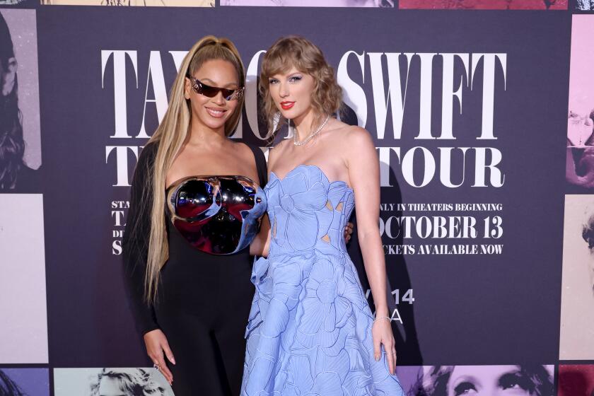 Beyoncé in a black body suit with a metallic breast plate and sunglasses next toTaylor Swift in a blue strapless dress