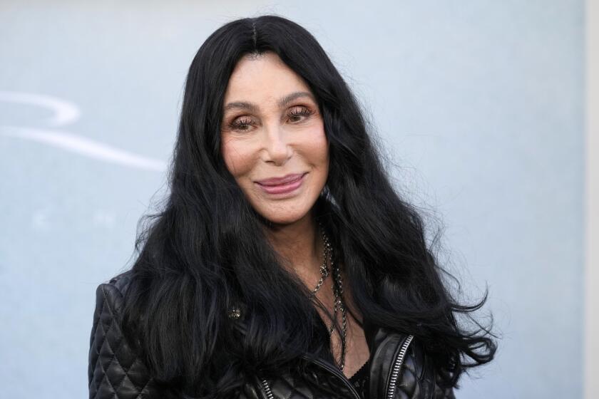 Cher smiles with her long dark hair parted in the middle while wearing a black leather jacket