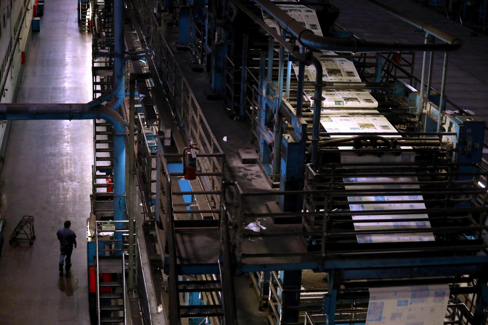 A pressman walks past presses where newspapers roll off in the final days of the Olympic printing plant.