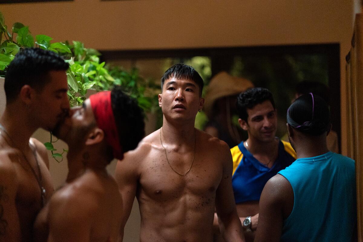 A shirtless man moves among chatting and kissing men.