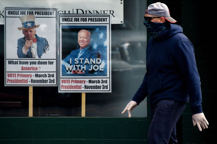 A man wearing a face mask walks past signs for Joe Biden's 2020 presidential campaign amid the coronavirus outbreak on May 11, 2020 in Alexandria, Virginia. (Photo by Olivier DOULIERY / AFP) (Photo by OLIVIER DOULIERY/AFP via Getty Images)