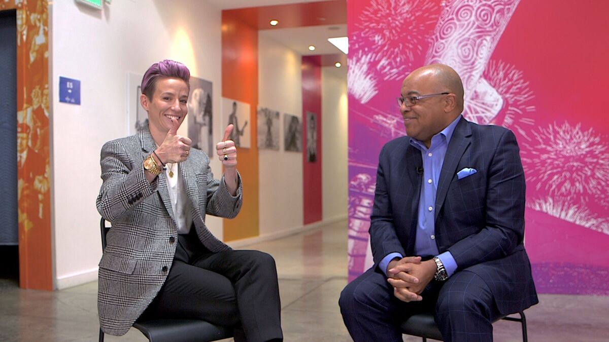Megan Rapinoe with Mike Tirico.during open mike photo sessions. NBCUniversal recently summoned 110 U.S. athletes to a West Hollywood studio, shepherding them through soundstages, photo shoots and recording booths, taping interviews for use during the Games and, just as important, gathering raw material for ads and promos right now.