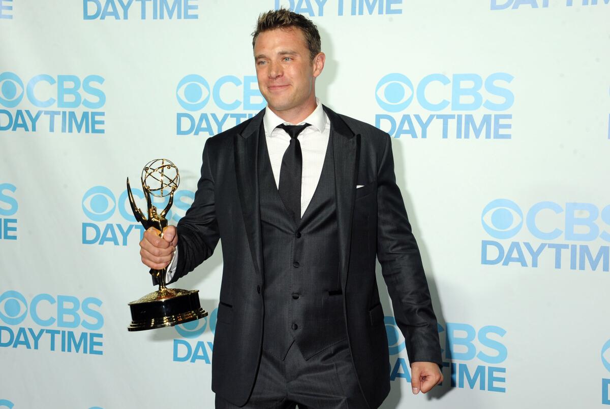Billy Miller wears a suit and holds his Daytime Emmy statuette.