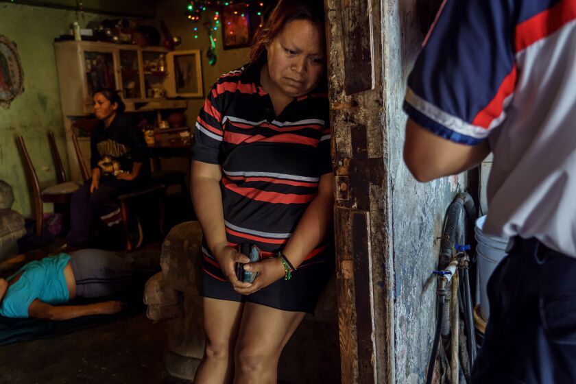 TIJUANA, BAJA CALIFORNIA -- WEDNESDAY, APRIL 29, 2020: As Sergio Garcia stands in the doorway to calmly explain the next steps after death, Georgina Barajas Rios, grieves for her mother who just passed away, Maria Ruiz Olmedo, 71, after she suffered from symptoms that match COVID-19 symptoms, at their home, in Tijuana, Mexico, on April 29, 2020. (Marcus Yam / Los Angeles Times)
