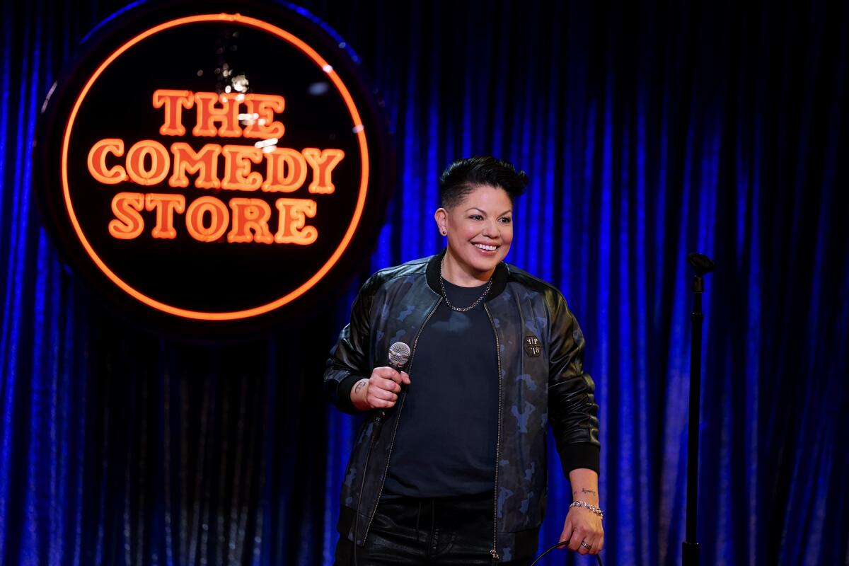 A smiling woman holds a microphone onstage at the Comedy Store.