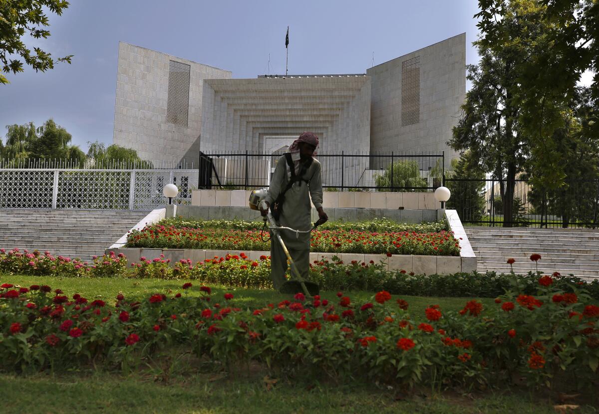 A worker mows the front lawn of the Supreme Court building where the hearing of the Hindu temple attack case is held in Islamabad, Pakistan, Friday, Aug. 6, 2021. A Muslim mob stormed a Hindu temple in a remote town in Pakistan's eastern Punjab province on Wednesday, damaging statues and burning down the temple's main door. The attack followed an alleged desecration of a madrassa, or religious school, by a Hindu boy earlier this week, police said. (AP Photo/Anjum Naveed)