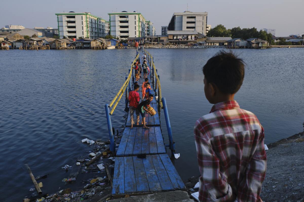 Boys walk across a makeshift bridge to reach their neighborhood, which lies below sea level in Jakarta, Indonesia. Jakarta, one of the world's most densely populated cities, is also one of the fastest-sinking cities in the world, due to out-of-control development and rising sea levels.