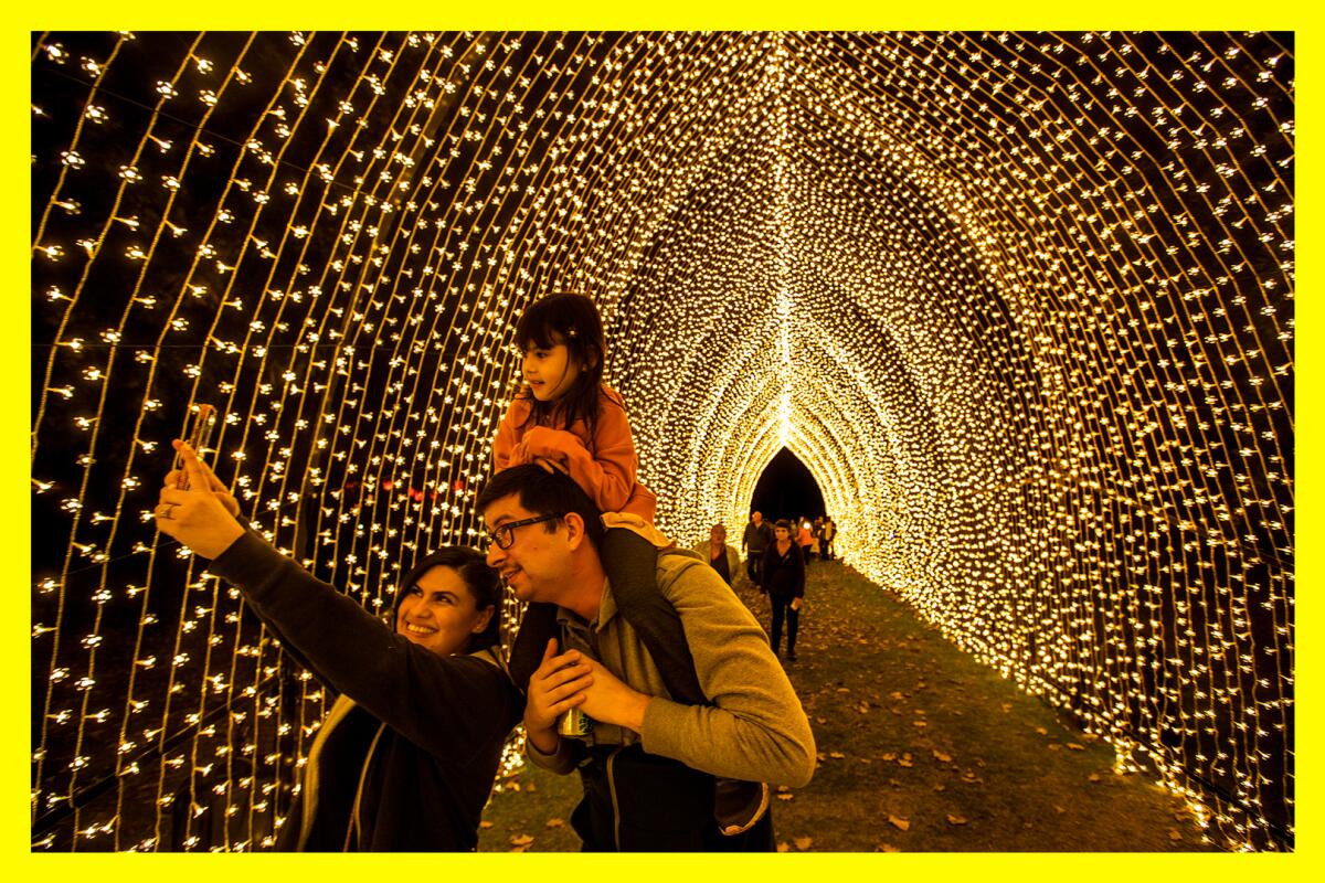 Three people take a nighttime selfie in a tunnel of holiday lights 