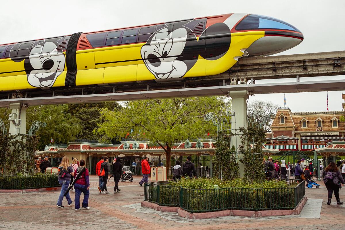 The monorail decorated with Mickey Mouse heads travels on a raised rail as while people pass below it.