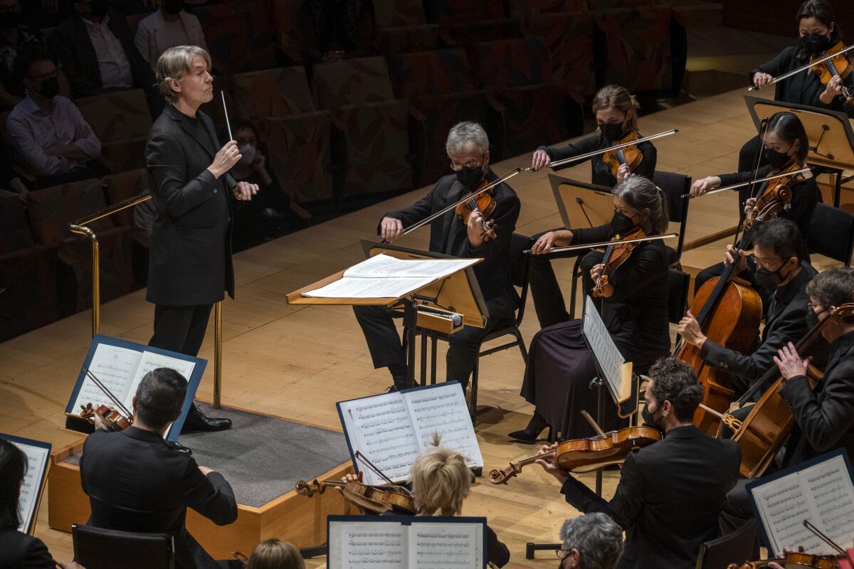 A conductor stands before a circle of seated musicians.