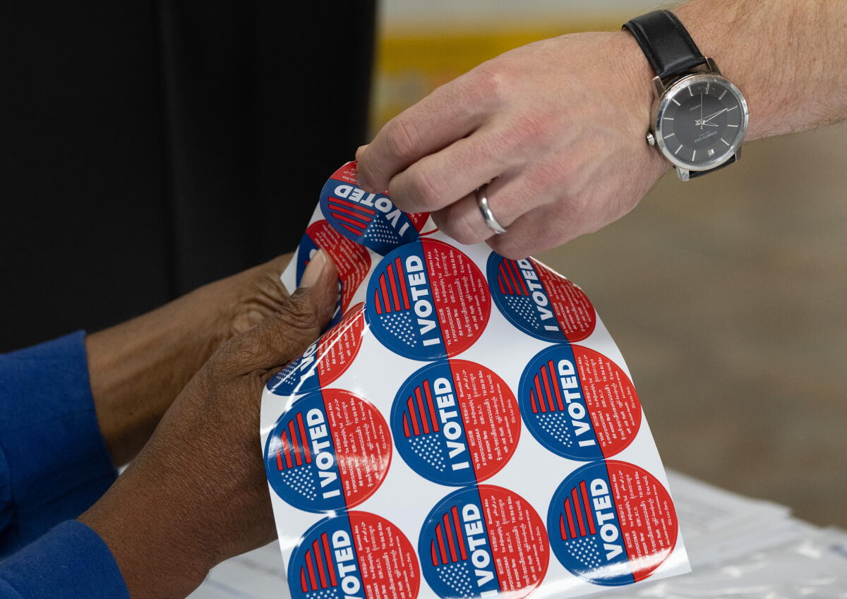 A sticker from a sheet of I Voted stickers is given to a voter dropping off a ballot