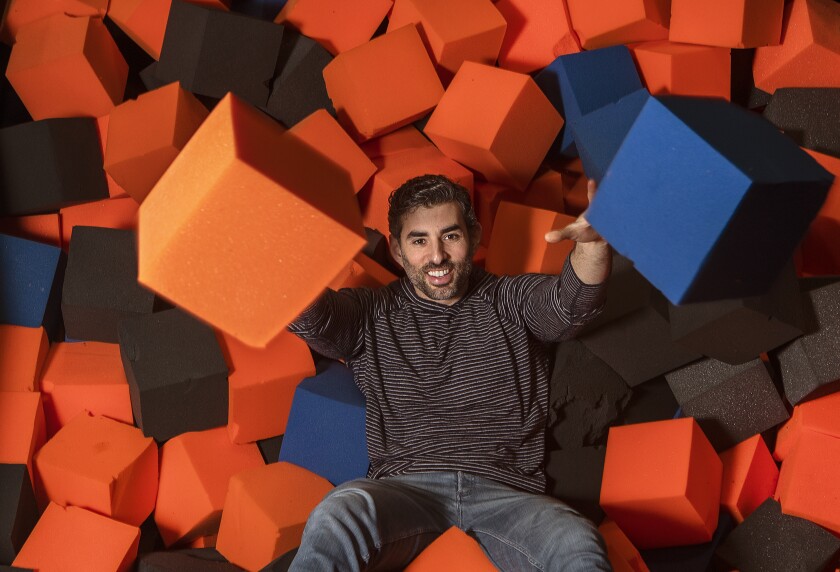 A man sits in a pit of foam cubes at an indoor trampoline park.