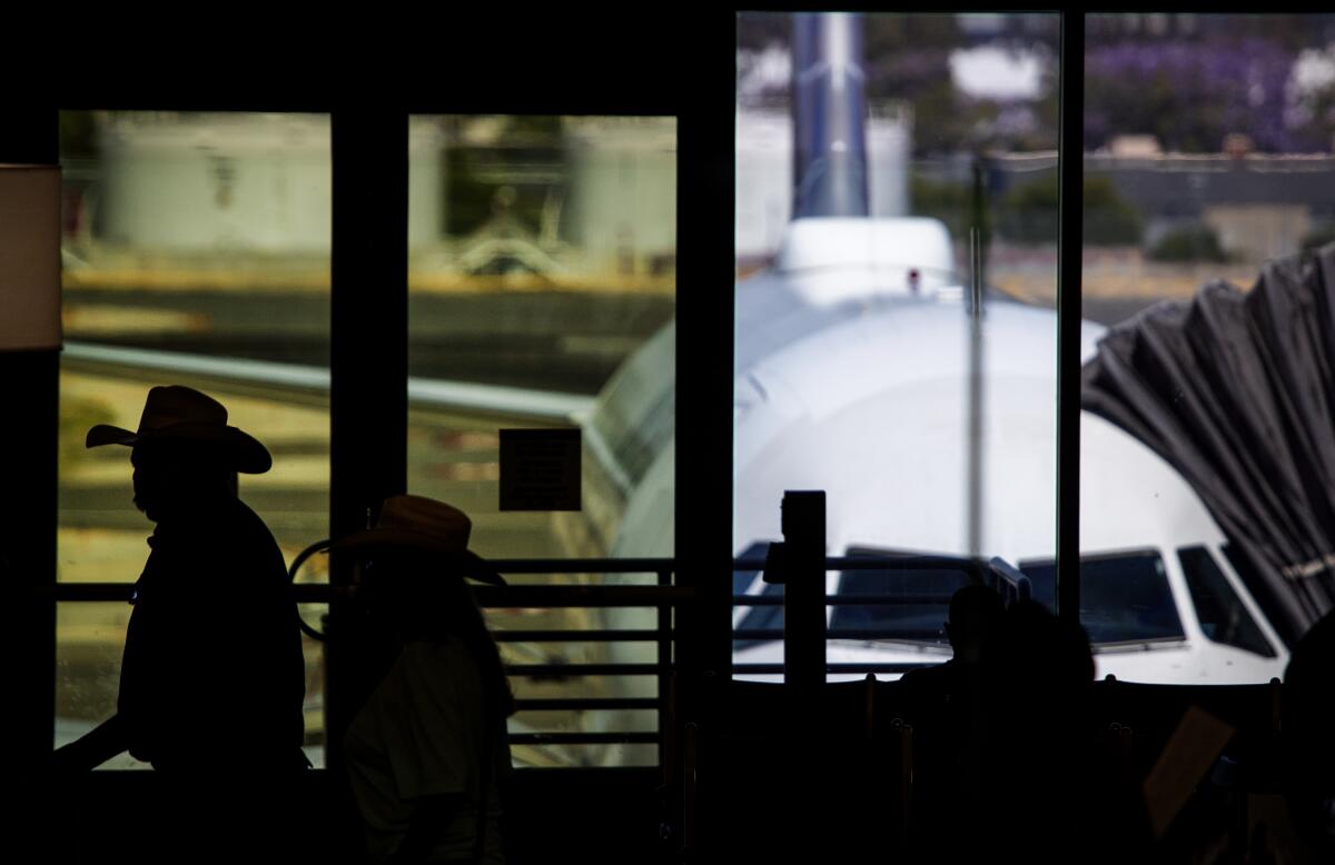 People walk in front of airport windows where a plane can be seen at the gate