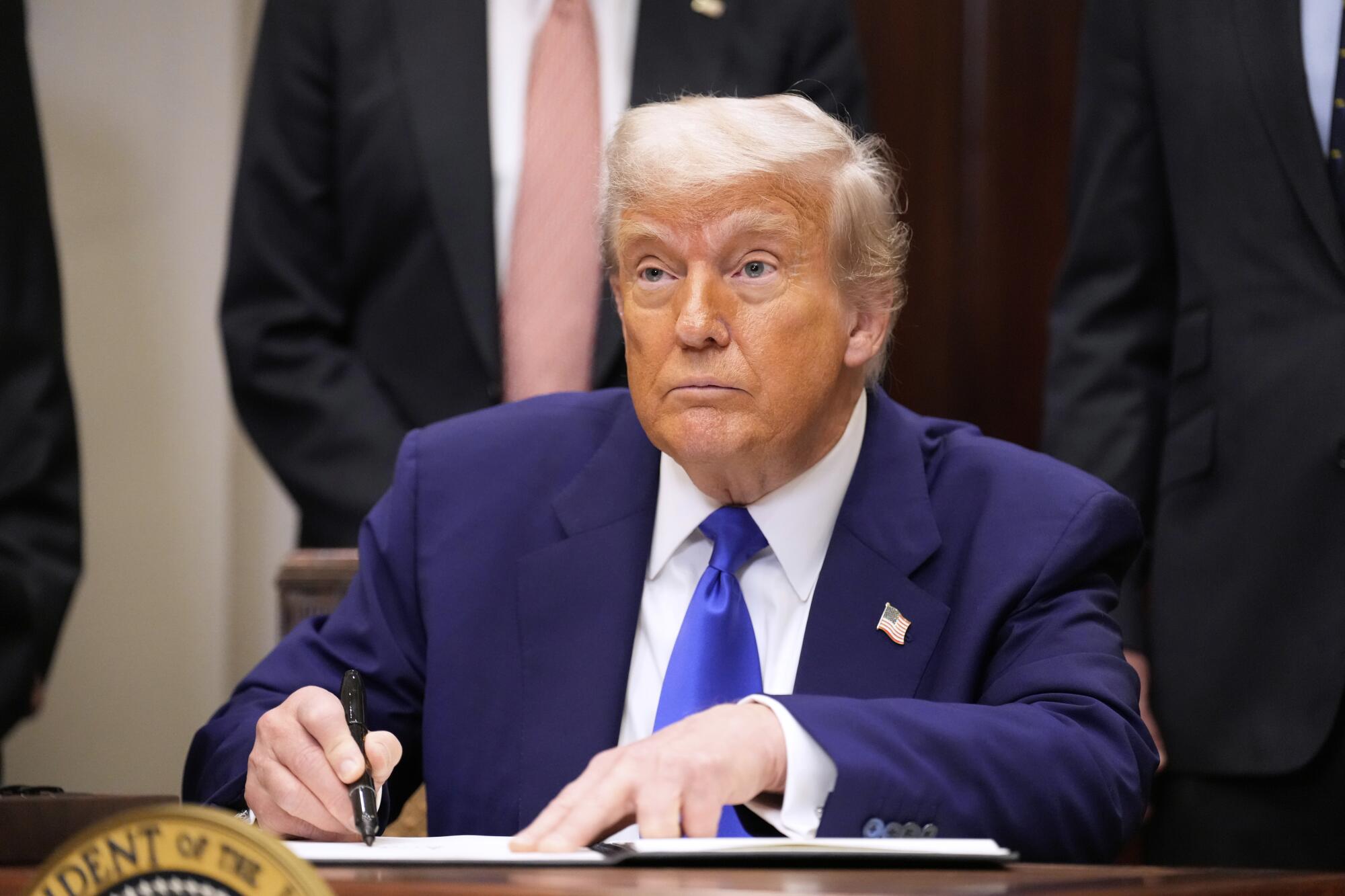 A man seated at a desk holds a pen.