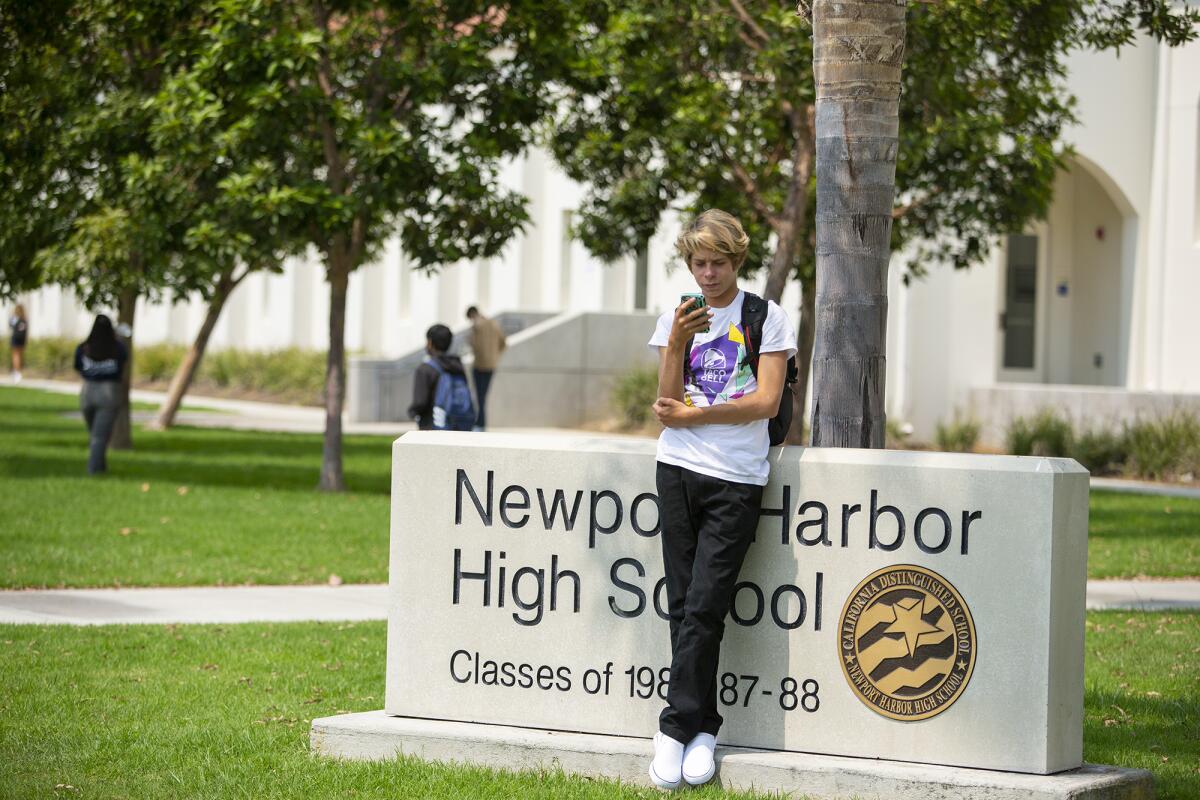 A student looks at his phone after school at Newport Harbor High School in 2021.